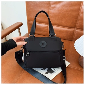 Detail of black nylon crossbody bag with rubber logo badge on a brown leather sofa