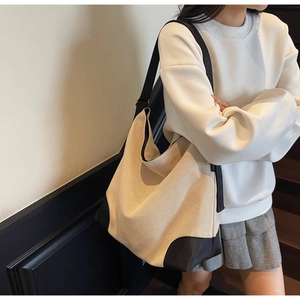 Side view of large beige canvas tote bag with black leather straps on a female model