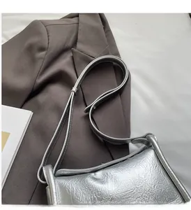 Detail of silver crossbody bag with cracked leather texture on a dark suit jacket