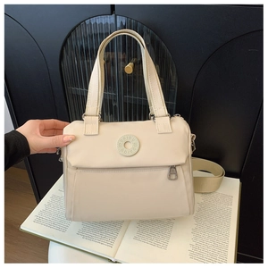 Detail of cream nylon crossbody bag with dual handles and round logo on an open book