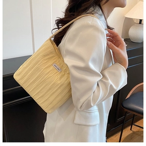 Detail showing vertical pleated texture and silver logo on yellow shoulder bag