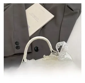 Detail of white crocodile embossed leather bag with lace bow and pearl handle