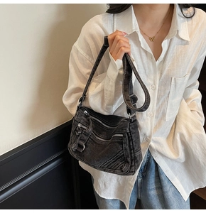 Close-up of black washed denim crossbody bag with multiple metal zippers on a model