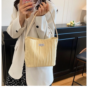 Detail of light yellow pleated canvas shoulder bag with textured fabric and white woven label