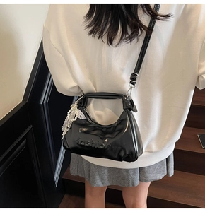 Detail of black glossy leather handbag with fashion embossing and pearl charm accessory