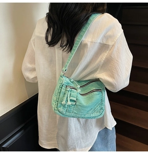Close-up of mint green denim crossbody bag showing pleated texture and silver zippers