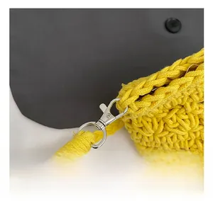 Detail of silver metal lobster clasp and yellow woven strap on a knitted bucket bag