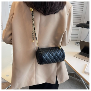 Détail d'un sac cylindrique matelassé noir avec chaîne dorée et détails en métal sphérique