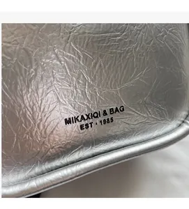 Detail of silver metallic handbag featuring unique pleated texture and brand logo print