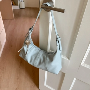 Detail of light blue lychee pattern leather shoulder bag with a silver heart pendant charm