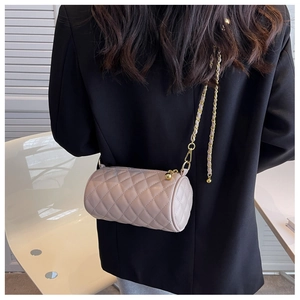 Détail du sac cylindrique matelassé avec chaîne dorée et boule en métal sur blazer noir
