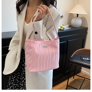 Detail of pink pleated canvas handbag with silver logo plate on white blazer outfit