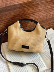 Sac à main en paille avec anses en cuir noir et bandoulière sur un fond de livre esthétique