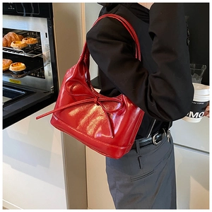 Detail of red glossy PU leather shoulder bag with stylish bow accent and sleek handle