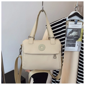 Detail of a beige nylon crossbody bag with wide handles and a circular logo patch