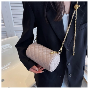 Détail d'un sac cylindrique beige matelassé avec bandoulière chaîne dorée sur blazer