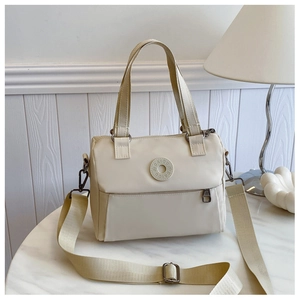 Detail of cream white nylon crossbody bag with dual handles and logo plaque on a table