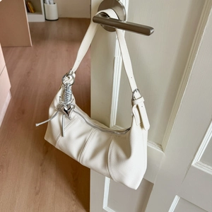 Detailed shot of a white lychee grain leather crescent bag with silver heart pendant charm