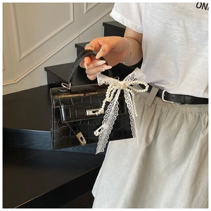 Detail of black crocodile texture handbag with white lace pearl bow and metal lock