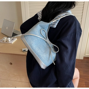Detail of denim tote bag with silver bow accent worn by model in a modern office setting