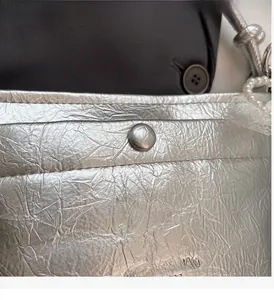 Detail of silver pleated texture on handbag with magnetic clasp and pearl lace accents