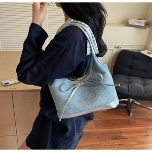 Detail of light blue denim tote with large silver bow and mirror-effect metallic trim