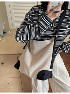 Minimalist canvas tote bag with black trim and wide strap shown in a lifestyle mirror selfie