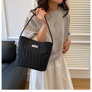 Detail of black pleated tote bag with white branding label and thin shoulder straps
