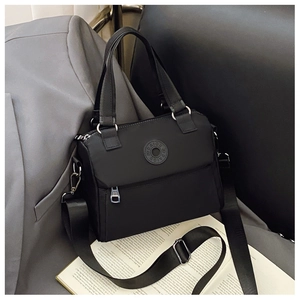 Close-up of black nylon bag with circular logo patch, silver zipper, and wide shoulder strap