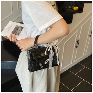Detail of black crocodile texture handbag with white lace bow and silver lock closure