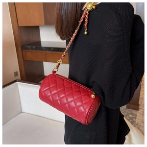 Détail du sac cylindre rouge matelassé avec chaîne dorée et boule d'or ajustable
