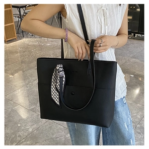 Detail of black pebbled leather tote bag with a geometric silk scarf on shoulder strap