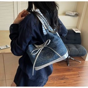 Detail of denim shoulder bag with a large silver bow and metallic trim on a model