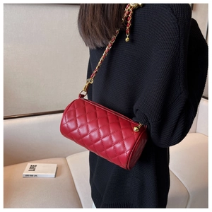 Détail du sac cylindre rouge matelassé avec chaîne dorée et finition en cuir texturé