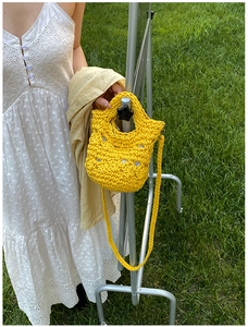 Detail of yellow hand-crocheted mini bucket bag with thick knit texture and woven strap