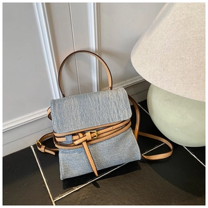 Close-up of light blue denim mini handbag with brown leather trim and golden metal buckles