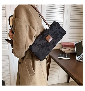 Détail d'un sac bandoulière en jacquard noir avec bordure en cuir marron porté au bureau