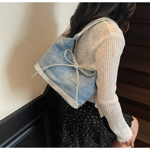 Detail of light blue denim tote bag with silver bow and metallic trim on shoulder strap