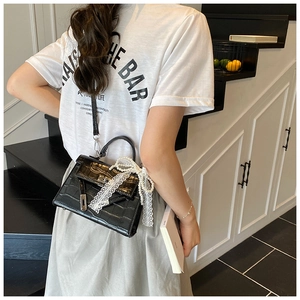 Detail of black crocodile texture handbag with lace bow and pearl charm on a white shirt