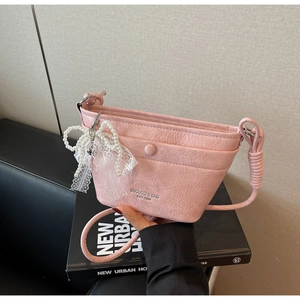 Detail of pink crossbody bucket bag with pleated texture and pearl bow ornament