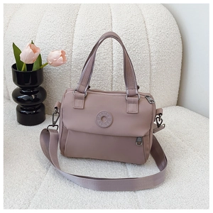 Detail of dusty pink nylon handbag with woven straps and logo emblem on a textured surface