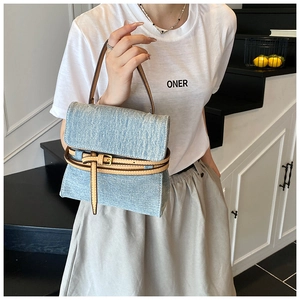 Detailed view of light blue denim handbag with brown leather straps and vintage metal buckles