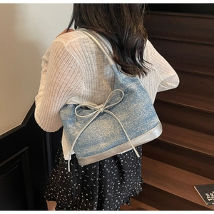 Close-up of denim tote bag with silver leather straps and fringe bow on wooden stairs