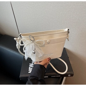 Detail of cream pleated bucket bag with pearl bow and lace charm on a luxury gift box