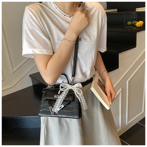 Detail of black crocodile pattern handbag with pearl lace bow and silver lock