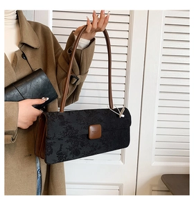 Détail du sac baguette noir gaufré de fleurs avec bandoulière en cuir marron