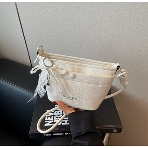 Detail of white pleated handbag with pearl bow charm and lace trim on book