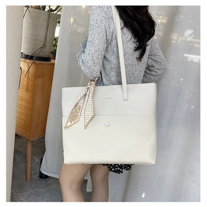 Close-up of white leather tote bag featuring a decorative silk scarf and metal snap detail