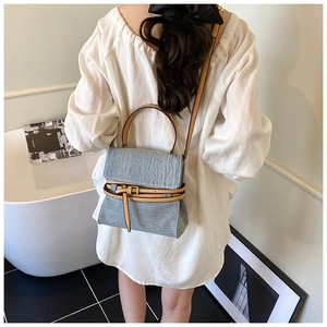 Detail of denim and brown leather strap on a shoulder bag worn by a model in a room
