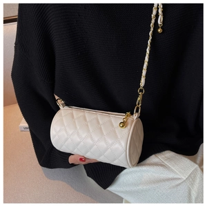 Détail du sac cylindrique blanc matelassé avec chaîne dorée sur un pull noir élégant